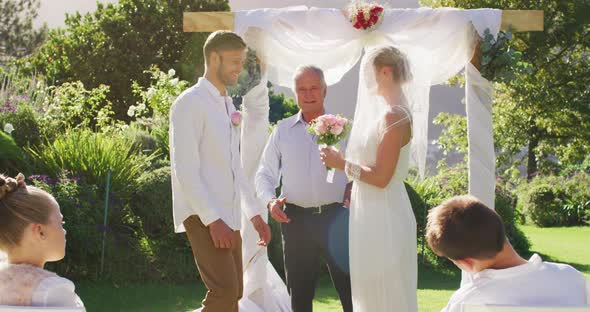 Caucasian bride and groom standing at outdoor altar with wedding officiant during ceremony alt