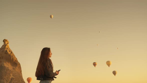 Young Woman Taking Video of Flying Hot Air Balloons in Morning