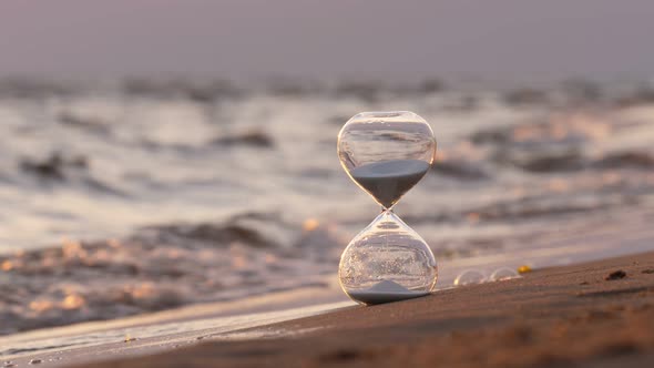 Hourglass stand on sand against wavy sea, selective focus alt