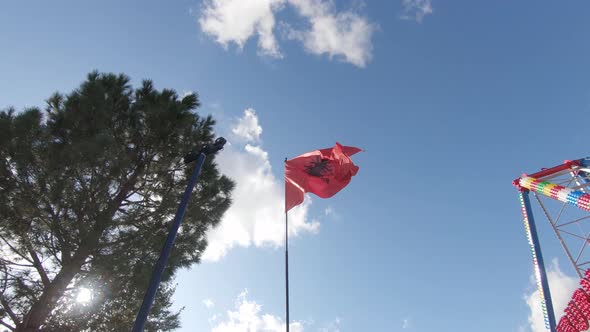 Proud Albanian Flag waving in the wind against the blue sky on top of flag pole alt