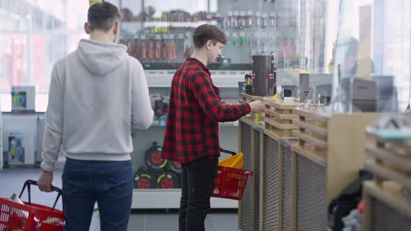 Side View of Young Male Customer Buying Goods at Cashier in Hardware Store alt