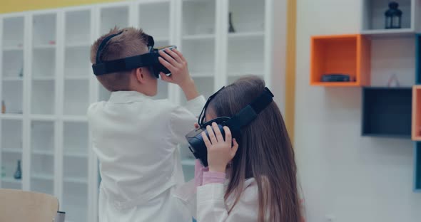 Little Boy and Little Girl in Virtual Reality Headset Standing in Classroom and Looking alt