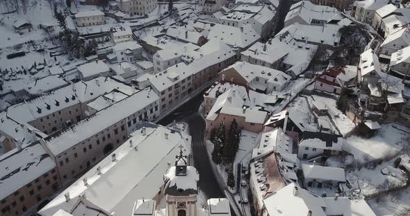 Flying above Christian Church and rooftops covered by snow in Mining town Banska Stiavnica, Aerial s alt