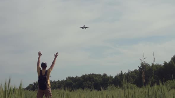 Happy Young Man Joyfully Greets an Airplane Flying in the Sky in a Wheat Field in the Summer at alt