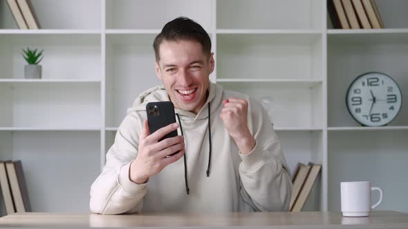 Surprised Man Winner Hold Smartphone Read Good News Amazed By Mobile Online Bet Bid Game Win at Home alt