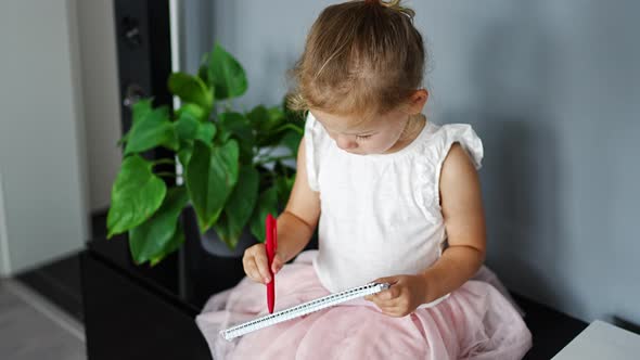Little Girl Draw or Write By Red Pencil at Home alt