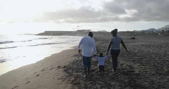 Happy african couple walking on the beach with little son alt