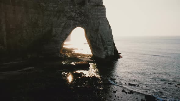 Drone Flying Along Epic White Cliffs of Normandy Shore Towards Natural Backlit Rock Arch  alt