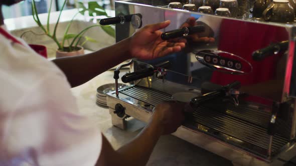 Midsection of african american male barista making coffee in coffee machine alt