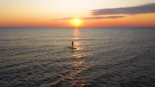 Young woman silhouette on a stand up paddle board. Sunset light in the water. alt