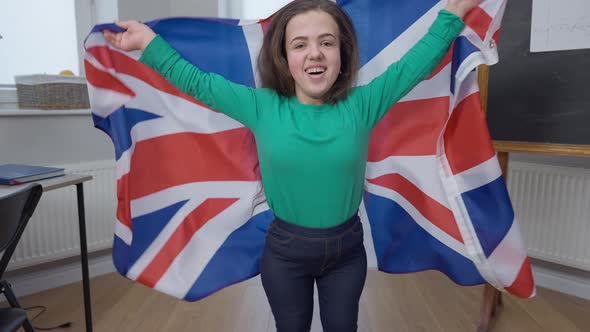 Portrait of Joyful Little Person Jumping with British Flag Looking at Camera Smiling alt