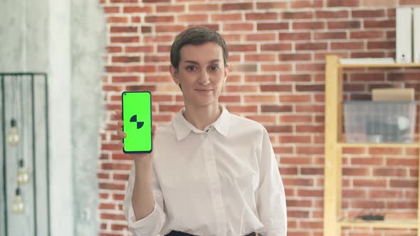Cute Business Woman a White Shirt Holds a Phone with an App and Looks at the Camera While Standing alt