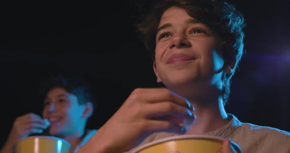 Boy watching a comedy movie at the cinema, he is eating popcorn and smiling