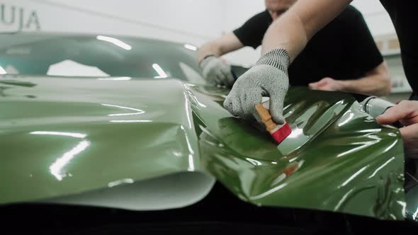 Two Men are Vinyl Wrapping a Car in Khaki Green Color Using Plastic Cards