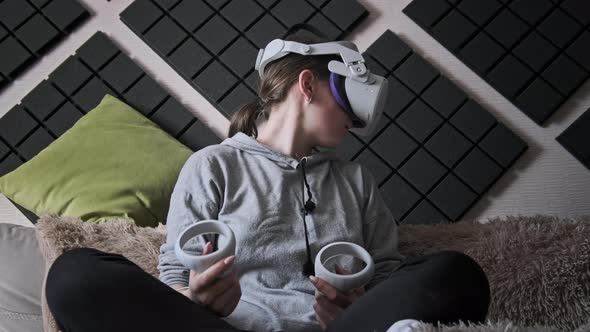 Young Woman in Virtual Reality Helmet Sitting on Sofa and Move Hands at Home alt