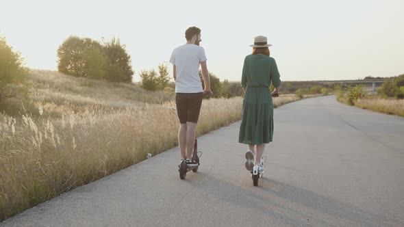Couple in Love Riding to Sunset Together on Electric Scooters on Asphalt Road alt