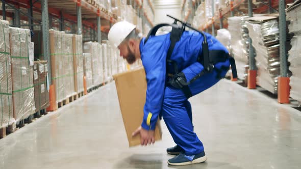 Storage Employee in Ergoskeleton Lifts a Package and Carries It alt