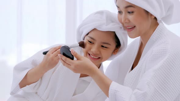 Mother with little daughter in bathrobes doing beauty treatment together in bedroom. alt