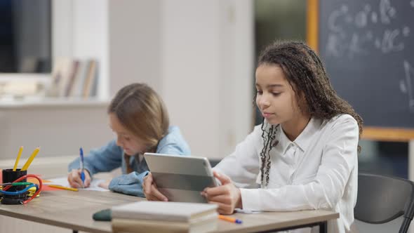 Joyful African American Schoolgirl Surfing Internet Messaging Online on Tablet with Blurred alt