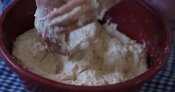 Baker hands kneading dough in flour on the ground.