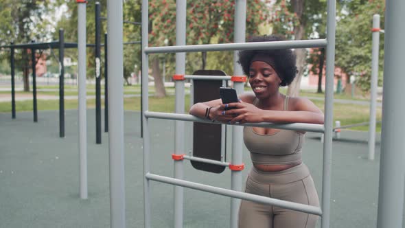 African American Woman Scrolling on Smartphone during Outdoor Training alt