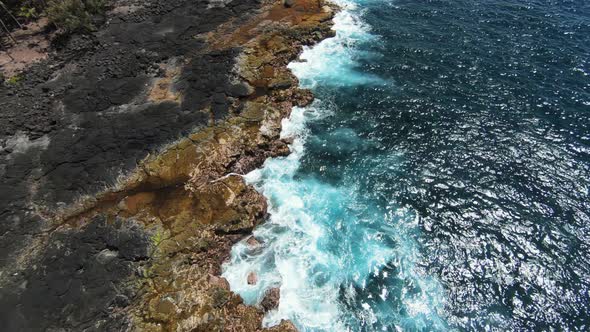 FPV slomo aerial rise above blue ocean crashing against orange basalt shoreline alt