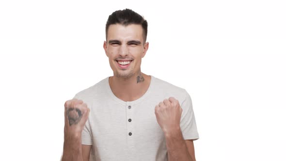 Horizontal Portrait of Brunette Tattooed Guy Wearing White Shirt Being Happy Clenching Fists Smiling alt