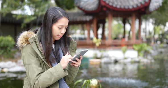 Asian Woman playing game on smart phone at china, Chinese pavilion garden alt