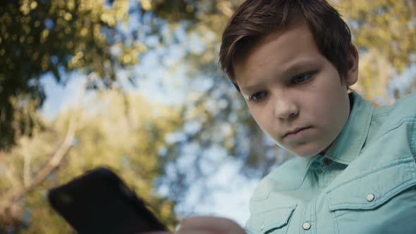Teenager Playing Video Games on His Smartphone Outdoors alt