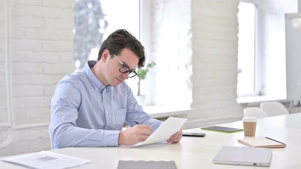 Serious Working Young Man Doing Paperwork in Office alt