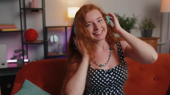 Happy Young Redhead Girl in Wireless Headphones Dancing Singing Listening Favorite Song at Home Room alt