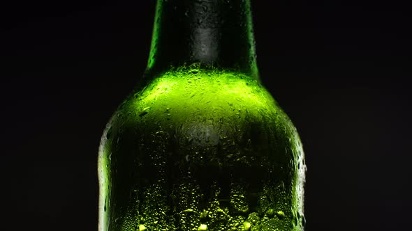 Beer Bottle Covered with Water Drops Rotating Against Dark Background alt