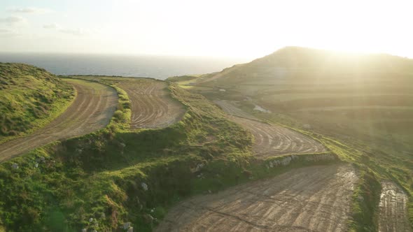 AERIAL: Sun Halo and Rays Shining in Camera While Drone Flies Above Green Malta Coastline alt