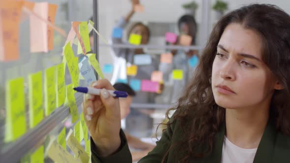 Young Woman Writing on Sticky Notes in Office alt