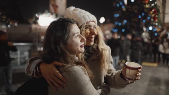 Portrait of Two Pretty Woman Hugging in a Middle of Christmas Celebration in European Town alt
