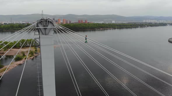 A Man Walks on a Rope Stretched Between the Supports of the Bridge at High Altitude.