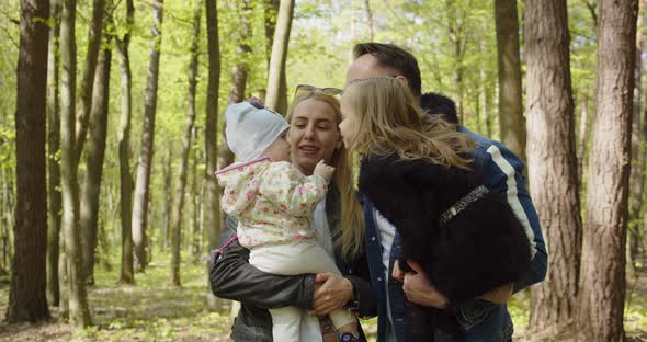 Happy Mom Dad With Small Children In His Arms In The Park. Girl Kissing Baby alt