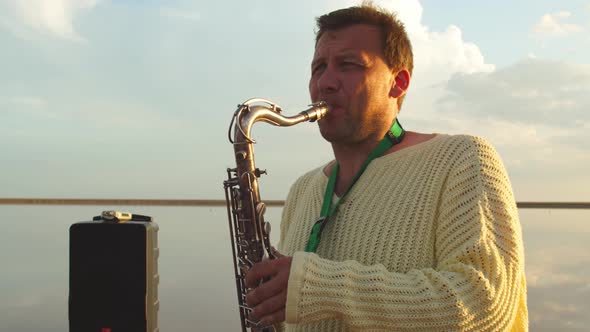 Portrait of a Man Playing Saxophone Outdoors in the Sea, Sunset Sky  alt
