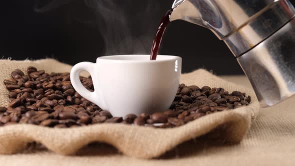 Pouring hot steaming coffee on cup from moka coffee machine. Jute background and coffee beans alt