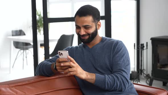 Cheerful Indian Guy Wearing Casual Outfit Messaging Texting on the Smartphone alt