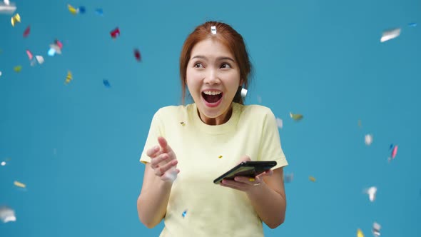 Asia lady using phone with positive expression under confetti rain and celebrate on blue background.
