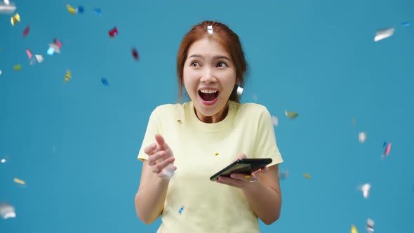 Asia lady using phone with positive expression under confetti rain and celebrate on blue background. alt