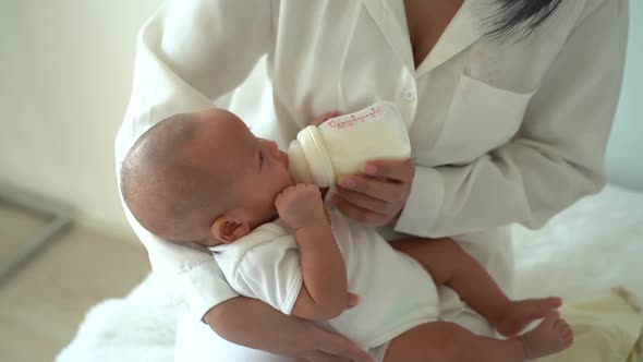Mother Holding and Feeding a Newborn Baby Boy From Bottle at Home alt