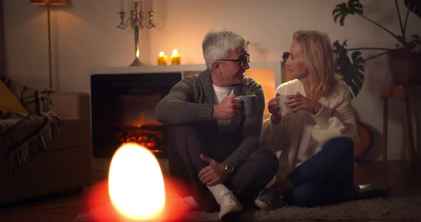 Happy Senior Couple Relaxing Together Near Fireplace and Drinking Coffee at Home alt