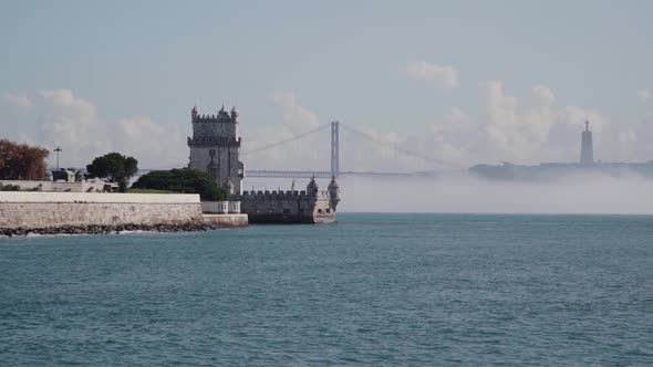 Portuguese Monument (Torre de Belem) with river in foreground and bridge in background alt