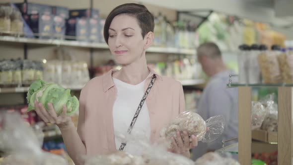Beautiful Young Woman Choosing Between Cabbage and Gingerbread Cookies. Portrait of Brunette Lady alt