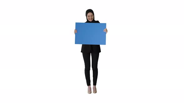 Smiling Arab Woman in Hijab Holding Blank Blue Poster and Looking at It on White Background alt