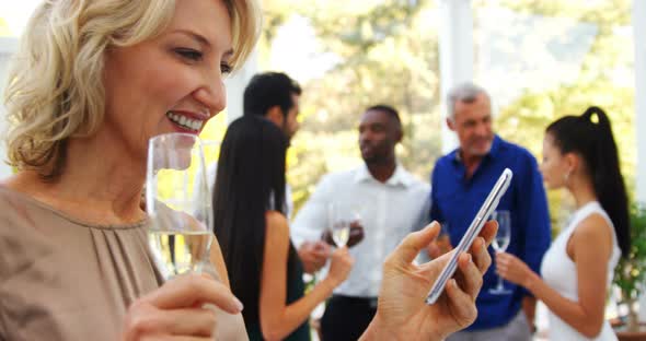 Smiling woman using mobile phone while friends interacting in background alt
