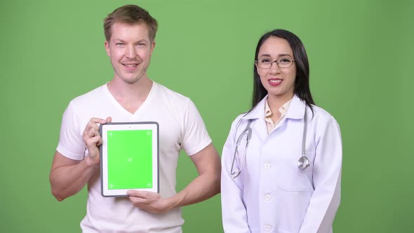 Young Asian Woman Doctor with Young Man Patient Showing Digital Tablet alt