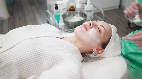 Girl Beautician Makes Facial Cleansing Procedure for Young Woman in Beauty Salon alt